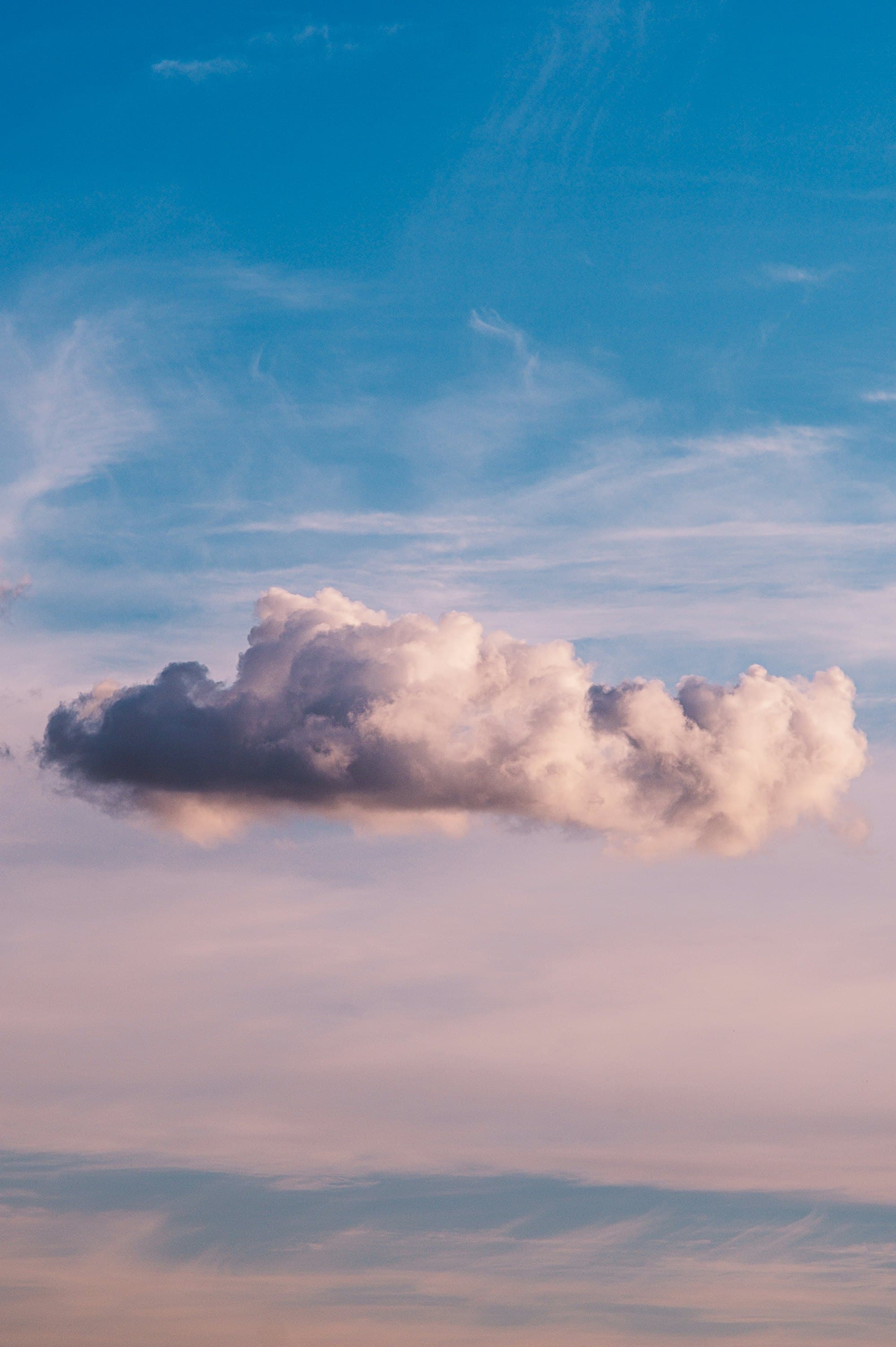 A single cloud lit from beneath at dusk, in a wide pale sky.